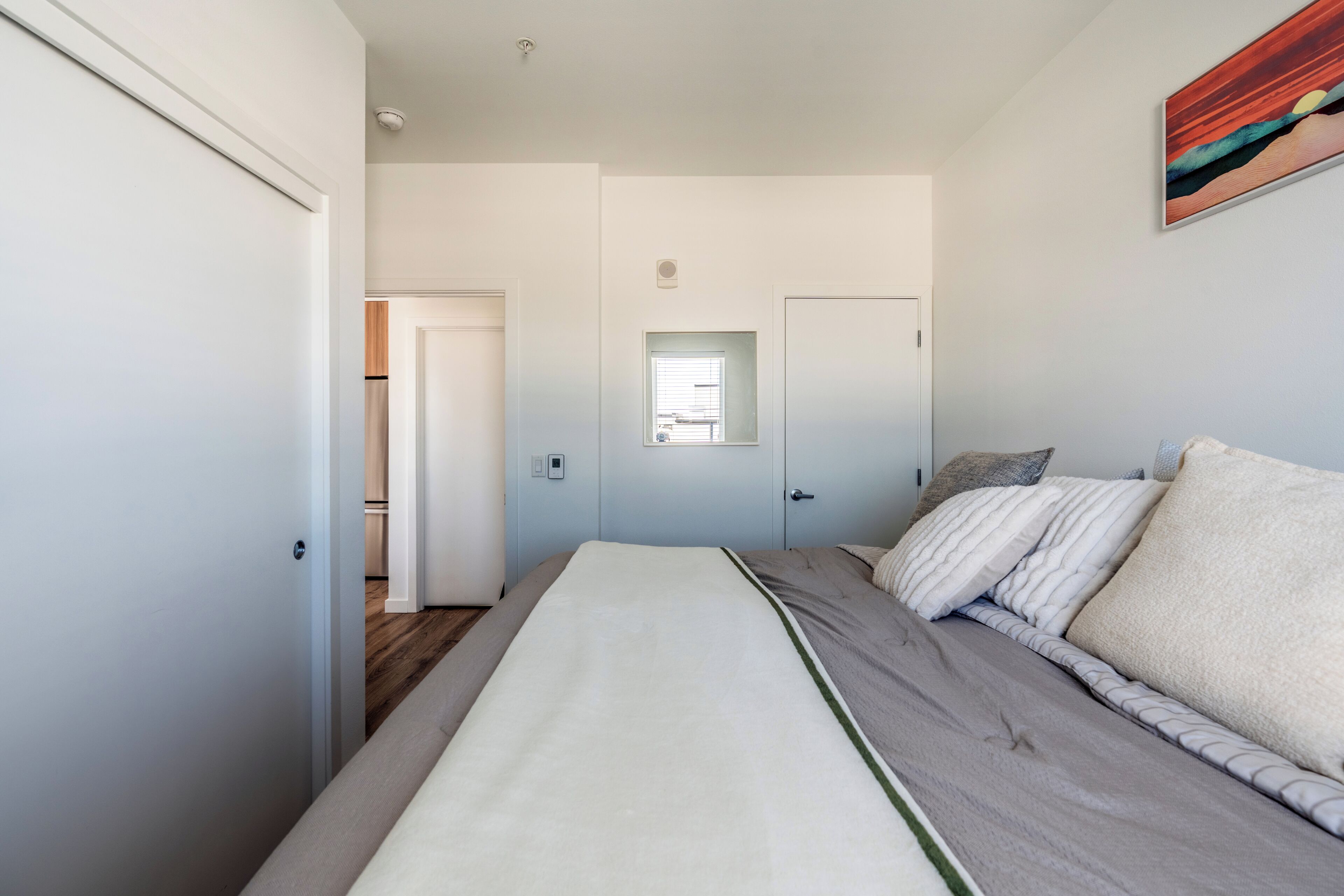 A bedroom with a bed, a window, and a door leading to another room.