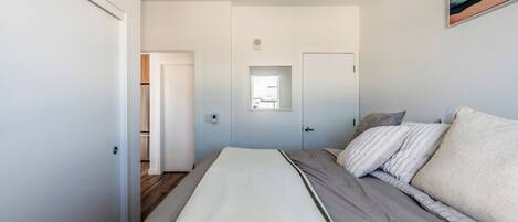 A bedroom with a bed, a window, and a door leading to another room.