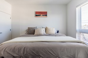 A bedroom with a bed, pillows, a painting, and a window with blinds.