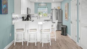 A modern kitchen with white cabinets, a central island with bar stools, a refrigerator, and a trash can.
