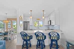 A modern kitchen with white cabinetry, a central island with bar stools, and pendant lighting.