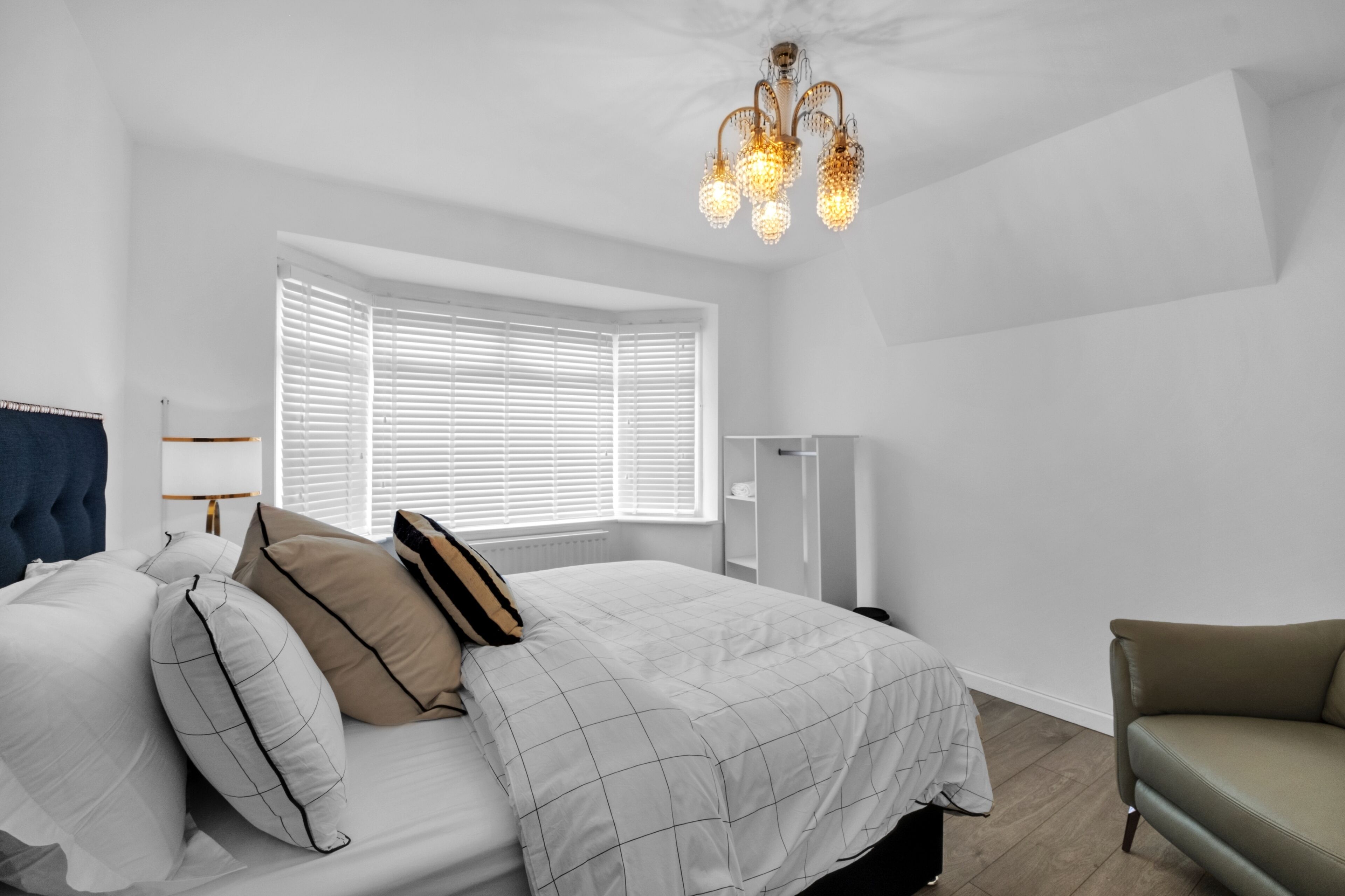 Ein Schlafzimmer mit Bett, Stuhl, Fenster mit Jalousien und einer Chandelüster.