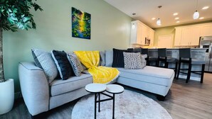A modern living room with a grey sectional sofa, a yellow throw blanket, and a round coffee table. - 2B/2B College Park home w/fenced patio yard, close to DT Orl & WP. Pet Friendly! (Orlando)