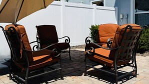 Two outdoor wicker chairs with cushions, a large beige umbrella, and a white fence in the background. - 2B/2B College Park home w/fenced patio yard, close to DT Orl & WP. Pet Friendly! (Orlando)