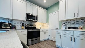 A modern kitchen with white cabinets, stainless steel appliances, and a wooden floor. - 2B/2B College Park home w/fenced patio yard, close to DT Orl & WP. Pet Friendly! (Orlando)