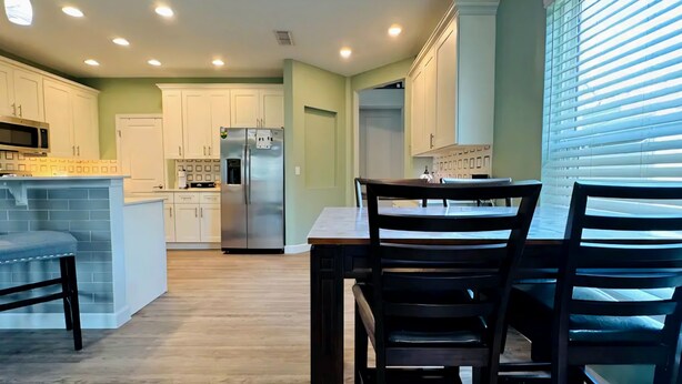 A modern kitchen with white cabinets, a stainless steel refrigerator, and a dining area with a wooden table and chairs. - 2B/2B College Park home w/fenced patio yard, close to DT Orl & WP. Pet Friendly! (Orlando)