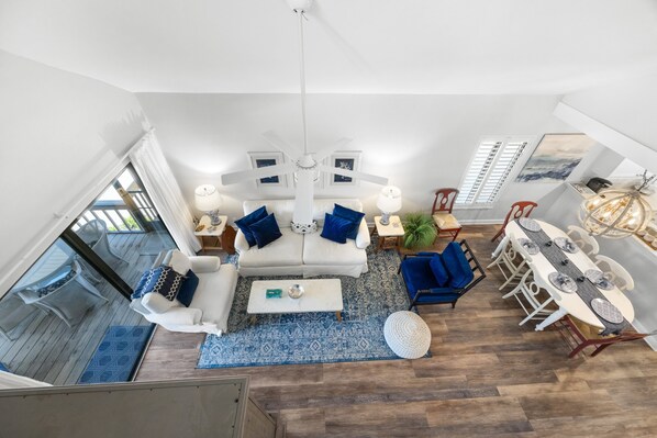 A spacious living room with a white sofa, blue cushions, a coffee table, and a dining area with a white table and chairs.