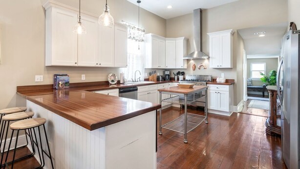 Une cuisine spacieuse avec des meubles blancs, un îlot central en bois et des luminaires suspendus.
