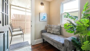 Un hall d’entrée accueillant, avec un banc, un coin salon confortable, un luminaire fixé au mur et une grande plante.