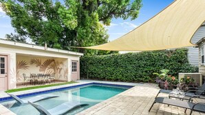 Un jardin avec une piscine, des meubles de patio et une grande voile d’ombrage.