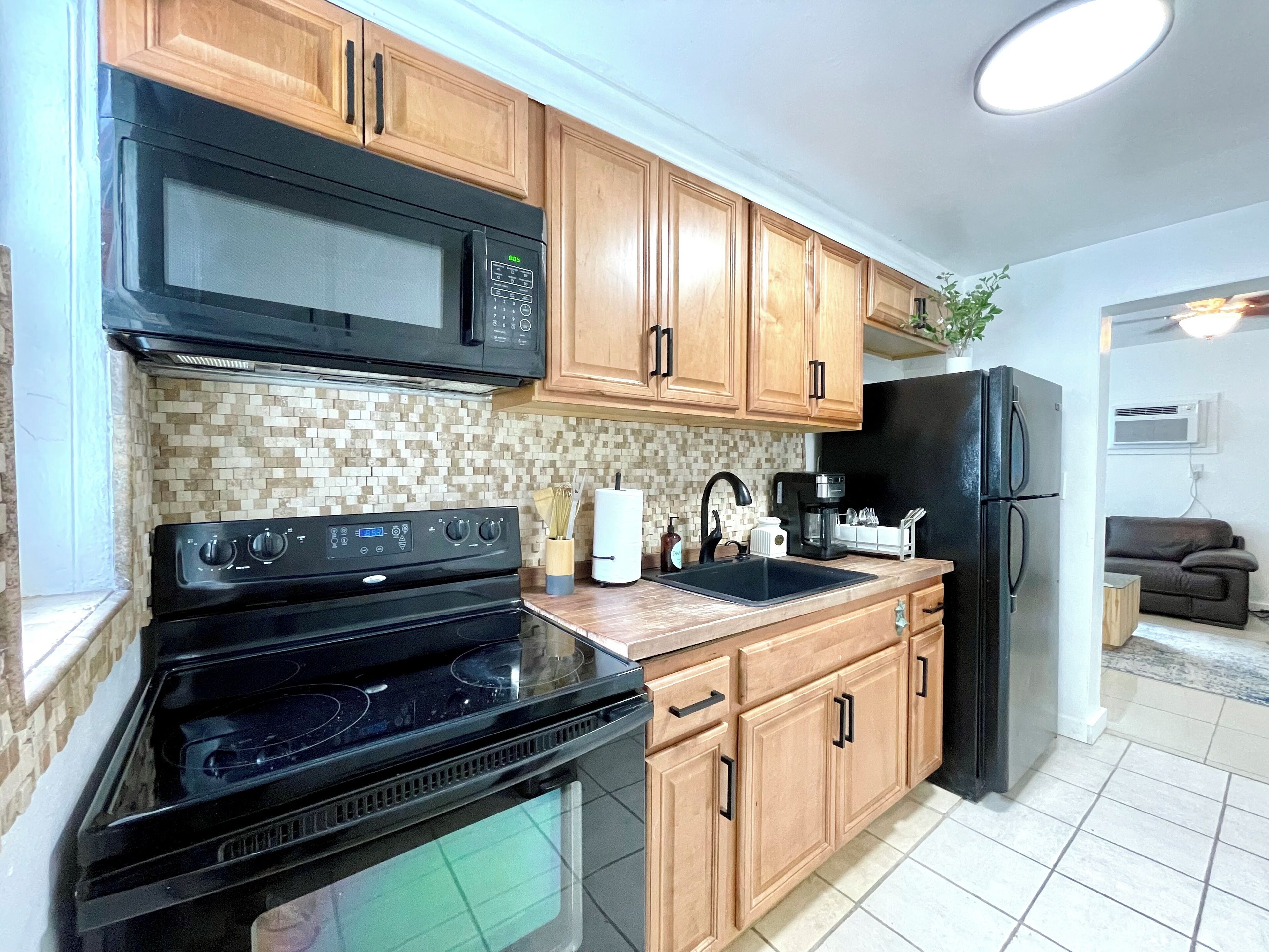 A kitchen with wooden cabinets, a black microwave, a stove, and a refrigerator.