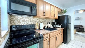 A kitchen with wooden cabinets, a black microwave, a stove, and a refrigerator. - 2237/U1-Top Pick-Beachfront-Downtown (Fort Lauderdale)