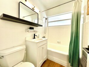A bathroom with a toilet, sink, mirror, and bathtub.