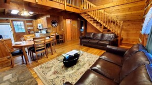 Ein Holzblockhaus-Interieur mit Essbereich, einer Couch und einer Treppe.
