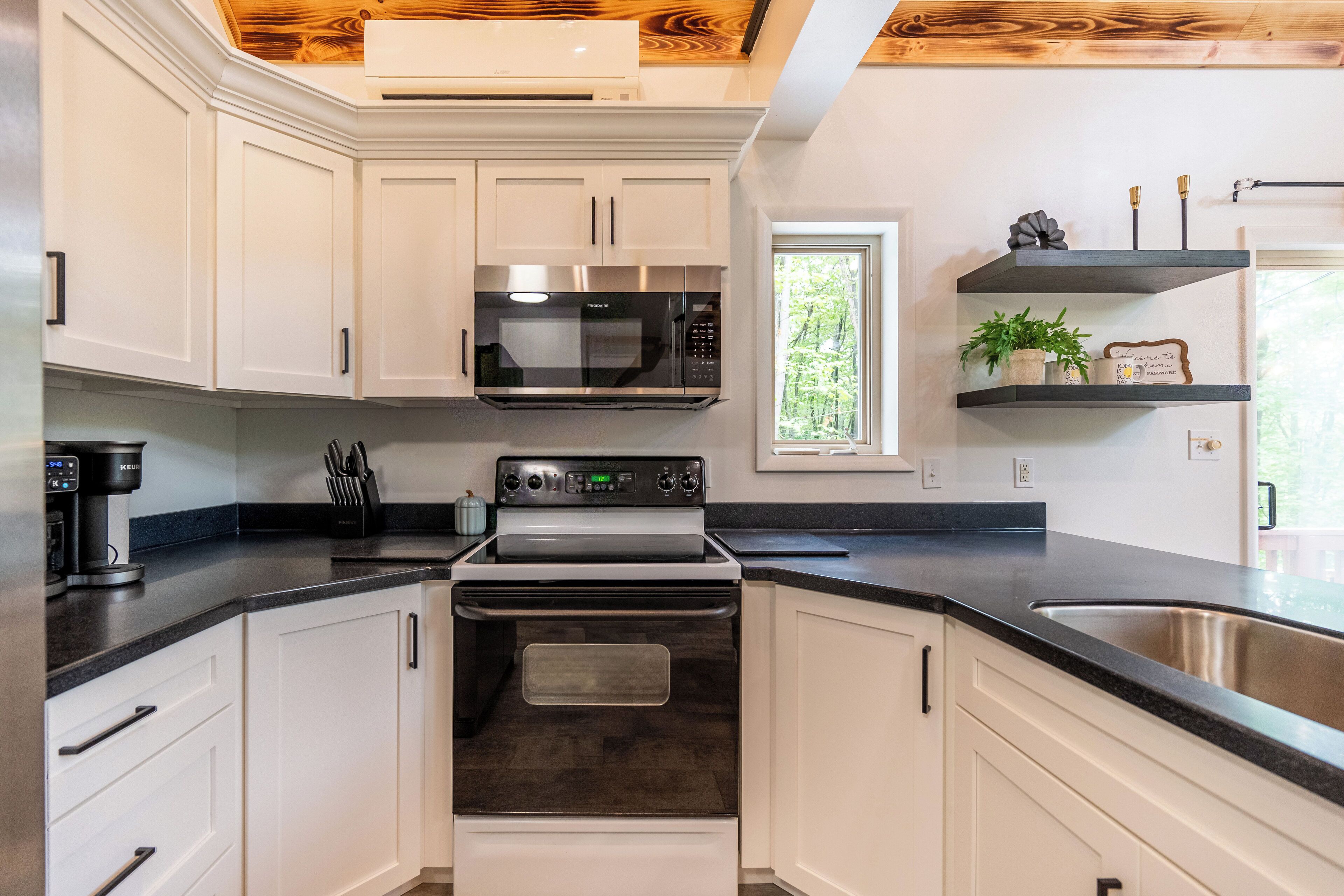 Een moderne keuken met witte kasten, een ingebouwde magnetron, een fornuis en een raam met uitzicht op de omgeving.