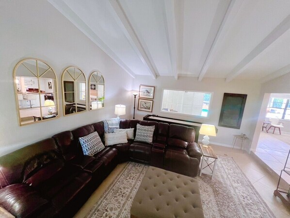 A living room with a dark leather sectional sofa, a round coffee table, and a large mirror on the wall. - Island living, steps to your own private beach! Beautiful home sleeps 6-8. (Vero Beach)