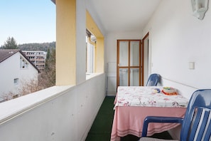 A balcony with a table, chairs, and a view of buildings and trees.