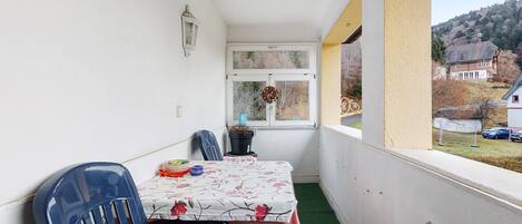 Un balcón con mesa, sillas, una planta en maceta y vistas a una casa y árboles.