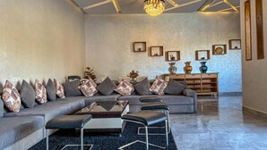 Un salon moderne avec un canapé d’angle, des poufs noirs, une table basse et un lustre.