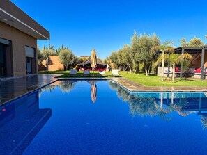 Ein Swimmingpool mit Liegestühlen und Sonnenschirmen, umgeben von Bäumen und einem Gebäude.