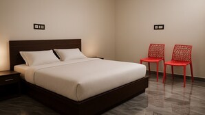 A modern hotel room with a large bed, a nightstand, and two red chairs. - hotel shraddha palace (Faizabad)