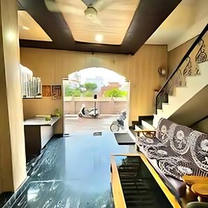 A modern interior with a central glass table, a sofa with patterned cushions, and a staircase leading to an outdoor area.
