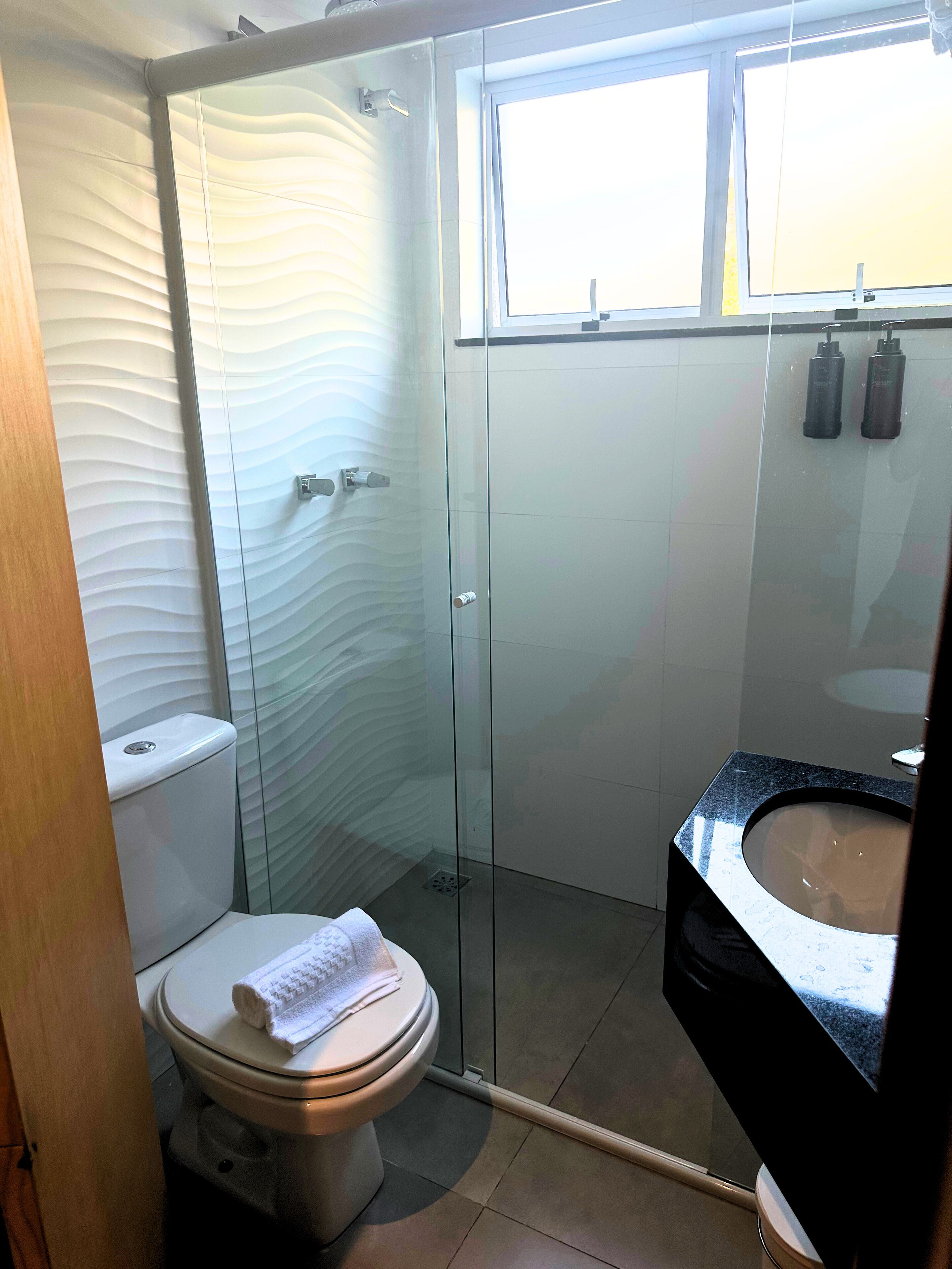 Een moderne badkamer met een douchecabine van glas, een toilet en een wastafel met een zwart aanrecht.