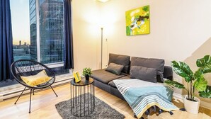 En moderne stue med en sofa, en lænestol, et lille bord med en plante og et stort vindue med gardiner.