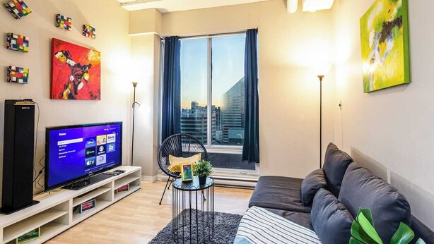 En moderne stue med et fladskærms-tv, en sofa, en lænestol og et vindue med gardiner.