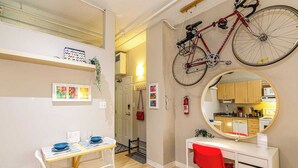 Et kompakt køkken med et rundt spejl, en cykel og et spiseområde med bord og stole.