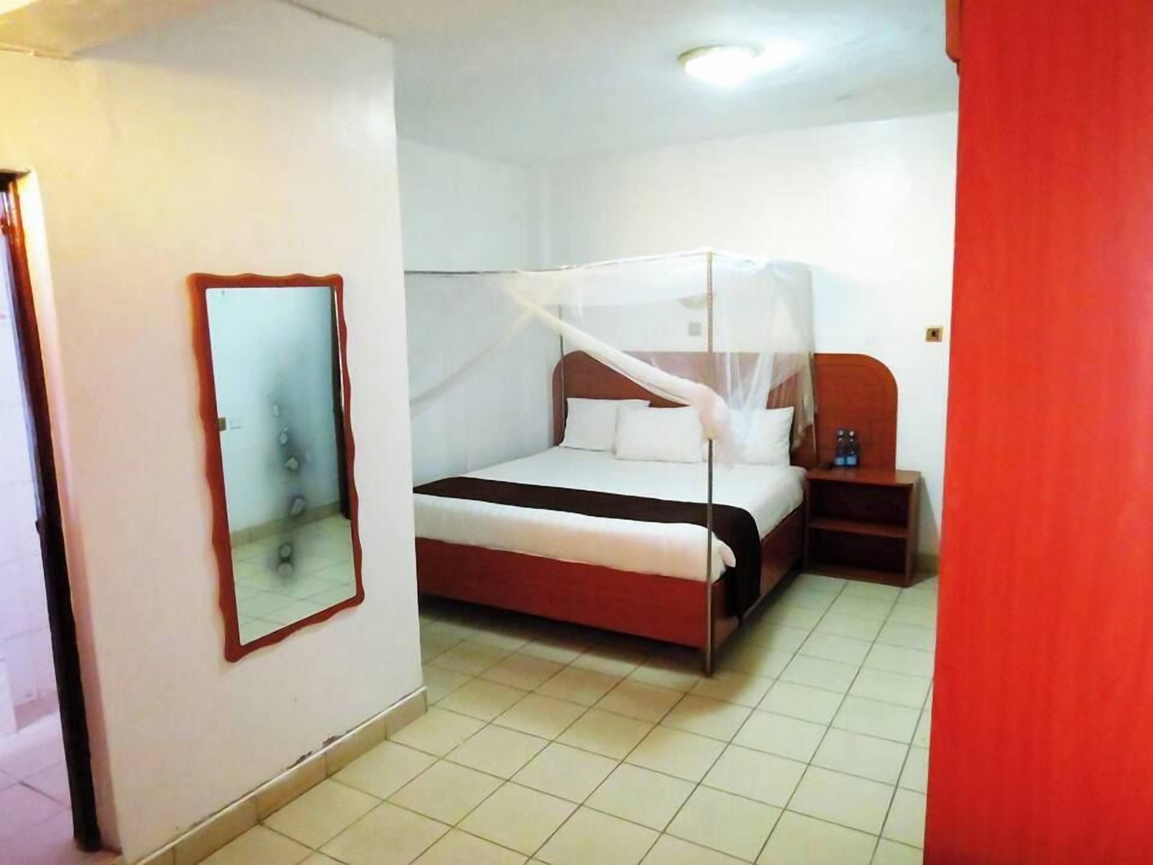Una camera d'albergo con un letto, un comodino, uno specchio e una parete rossa.