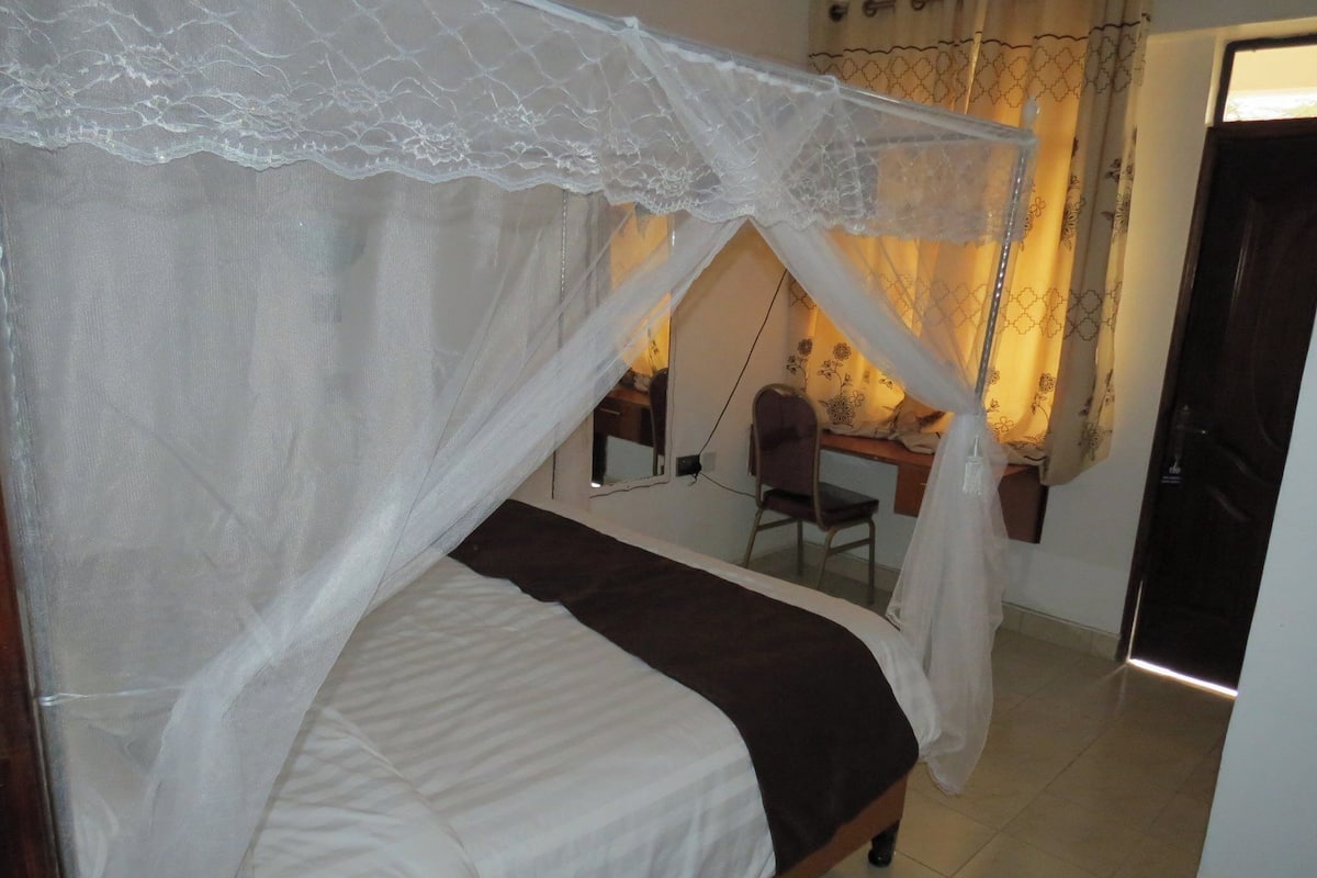 Quarto com cama sob dossel, escrivaninha com cadeira e porta.