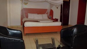A bedroom with a bed, a glass coffee table, two black leather chairs, and a red door.