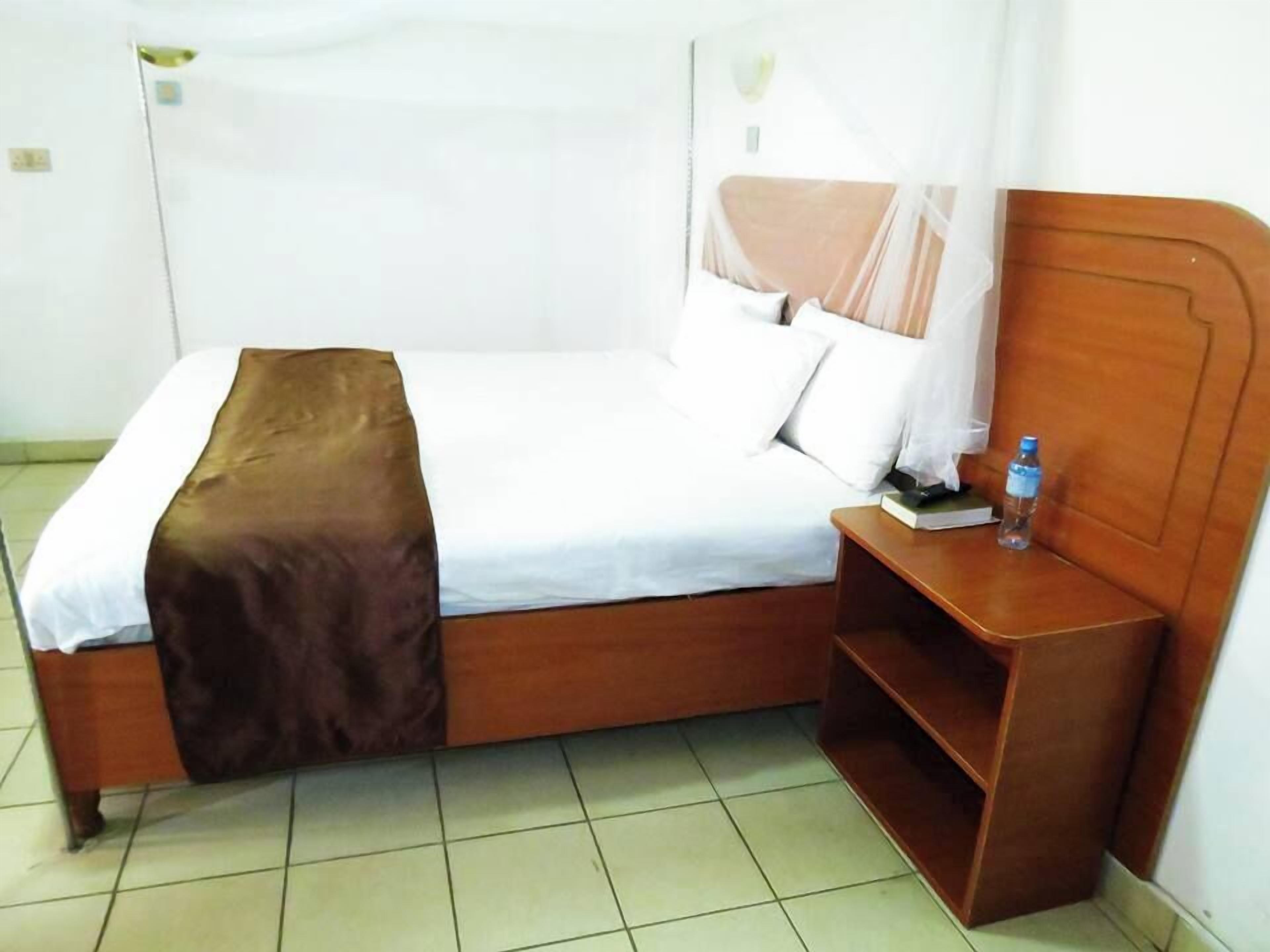 A hotel room with a bed, a nightstand, and a water bottle on the nightstand.