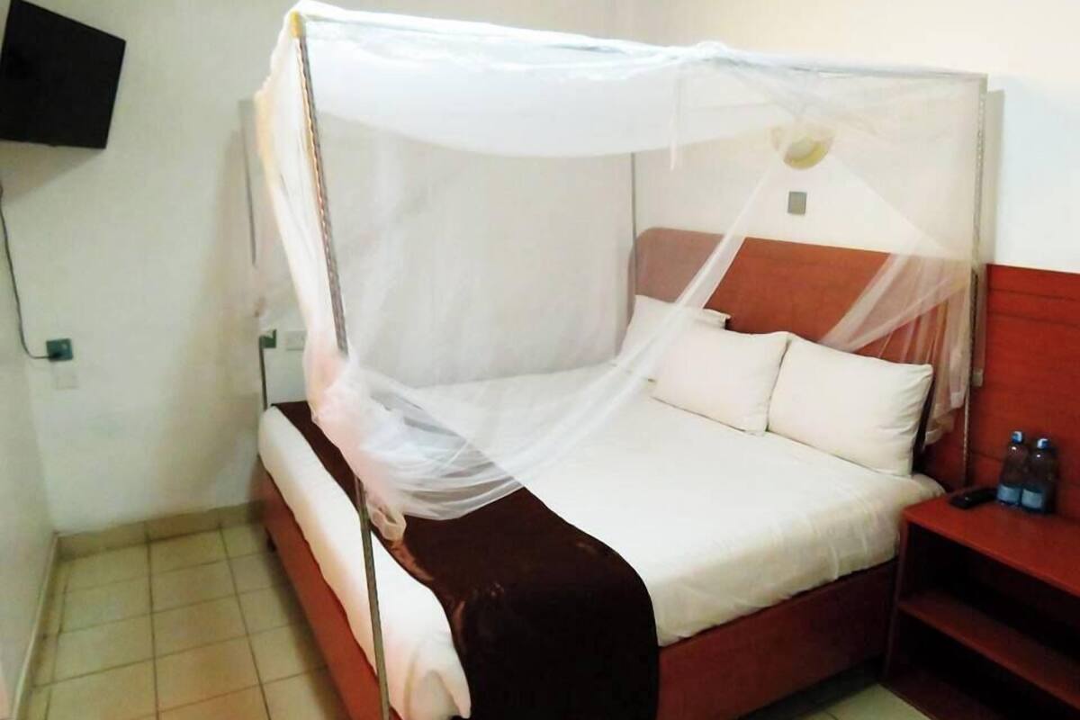 Uma cama com dossel branco, cabeceira de madeira e mesa de cabeceira com duas garrafas.