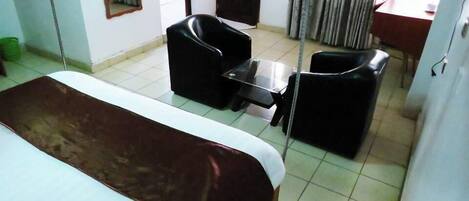 A hotel room with a bed, two black chairs, a small table, and a window with curtains.