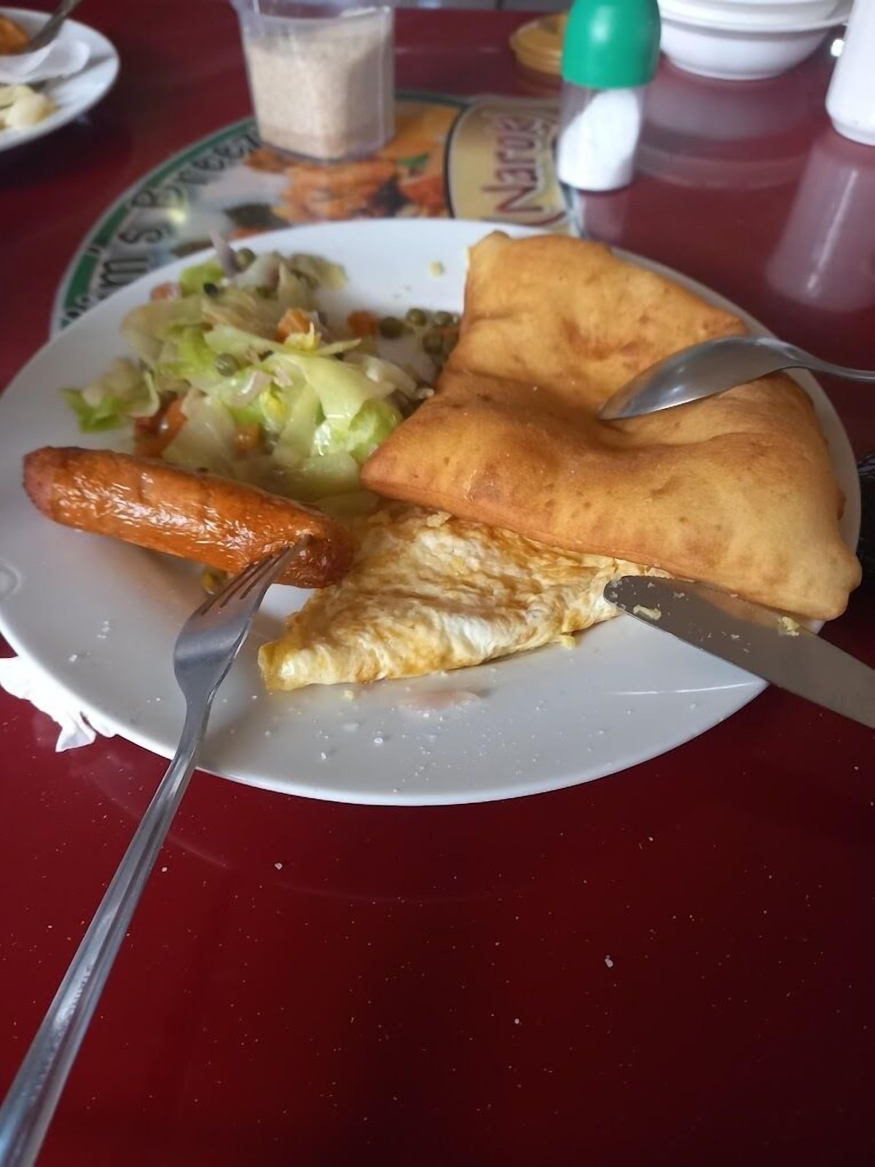 Un plato con una porción de pizza, una salchicha y una ensalada sobre una mesa roja.