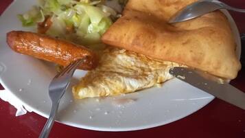 Un plato con una porción de pizza, una salchicha y una ensalada sobre una mesa roja.
