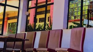 A row of chairs and a table in a room with large windows and a view of buildings outside.