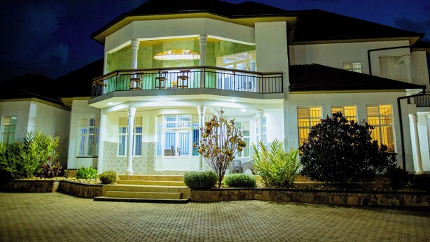 A two-story house with a balcony, a well-lit entrance, and a paved driveway.