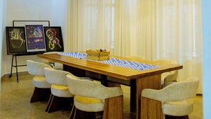 A dining area with a long wooden table, six chairs, a hanging light fixture, and framed artwork on the wall.