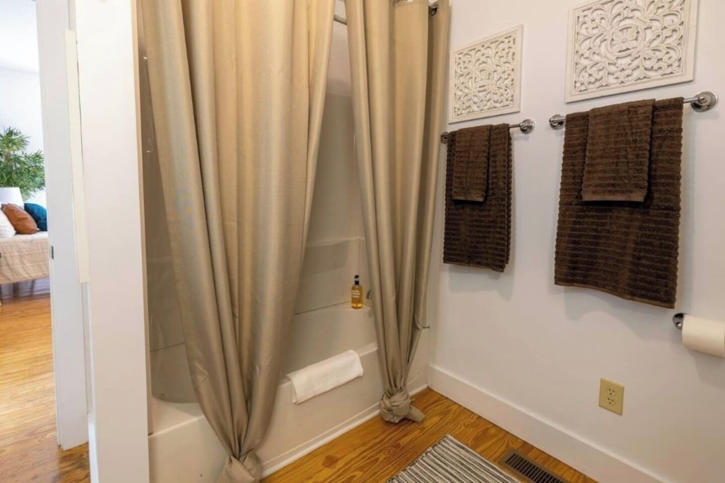 A bathroom with beige curtains, a bathtub, and two towels hanging on a towel rack.