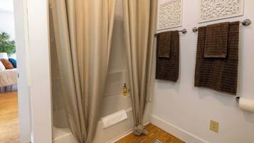 A bathroom with beige curtains, a bathtub, and two towels hanging on a towel rack.