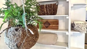 A hanging plant with a rustic pot, a woven basket, and a wooden tray on a white shelf.