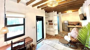 A cozy interior with a wooden ceiling, a dining area with a bench and chair, a kitchen with a refrigerator, and a large window.