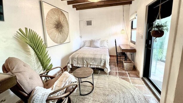 A cozy bedroom with a bed, a chair, a small table, and a large window.