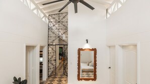 A hallway with a checkered floor, a decorative metal partition, a ceiling fan, and a mirror with a wooden frame. - Hacienda Oro Verde (San Jerónimo)