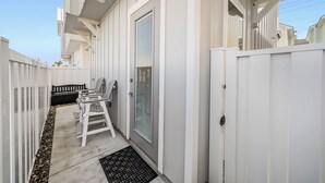 Un étroit couloir extérieur, bordé d’une clôture en bois peinte en blanc, avec un banc et une porte dotée d’un panneau de verre.