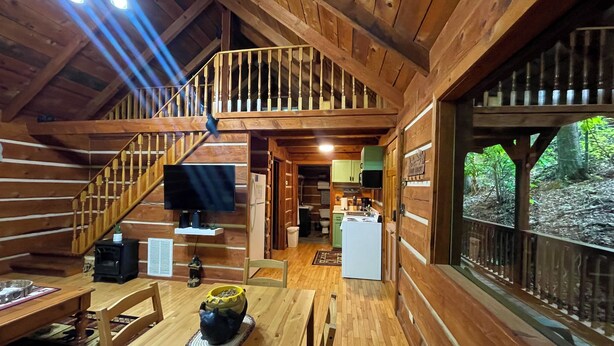 A cabin with a wooden interior, a staircase, a TV, a kitchen, and a view of the forest. - Hidden Treasure (Sevierville)