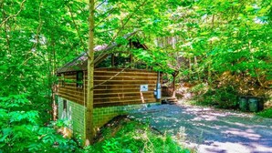 A rustic cabin with a wooden exterior, a brick foundation, and a small porch. - Hidden Treasure (Sevierville)